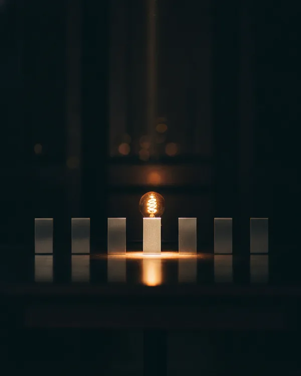 A row of small blank metal plates standing on edge in a dark room, the centre one lit brighter than the rest.