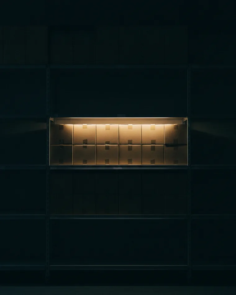 A dark retail shelf after closing with one section lit from within and plain unlabelled boxes arranged on it.