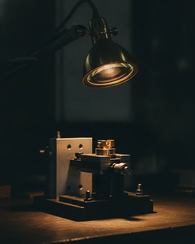 A test jig on a dark bench holding one component clamped under a magnifier arm.