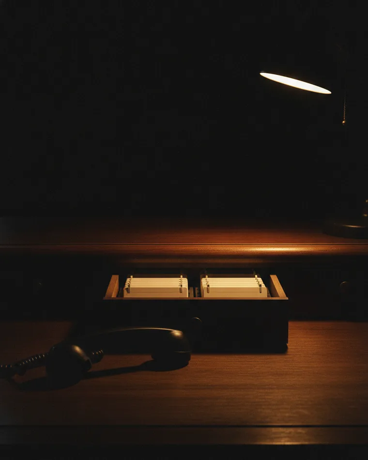 An open rolodex-style drawer of blank cards on a dark desk beside a telephone handset.