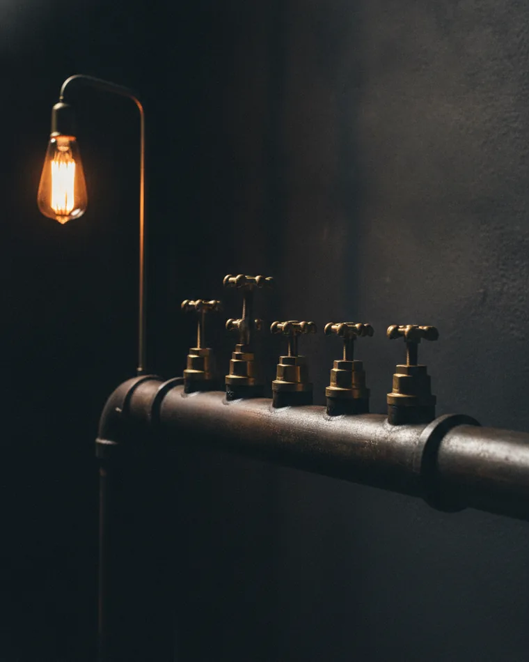 A bank of small brass valves on a dark pipe run, one handle turned open.