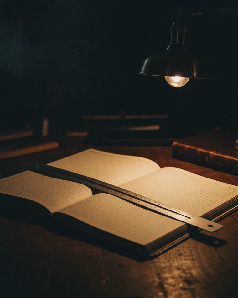 A large blank ruled ledger open flat on a dark table with a straight edge laid across the columns.