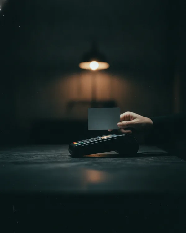 A plain bank card held above a payment terminal on a dark counter.