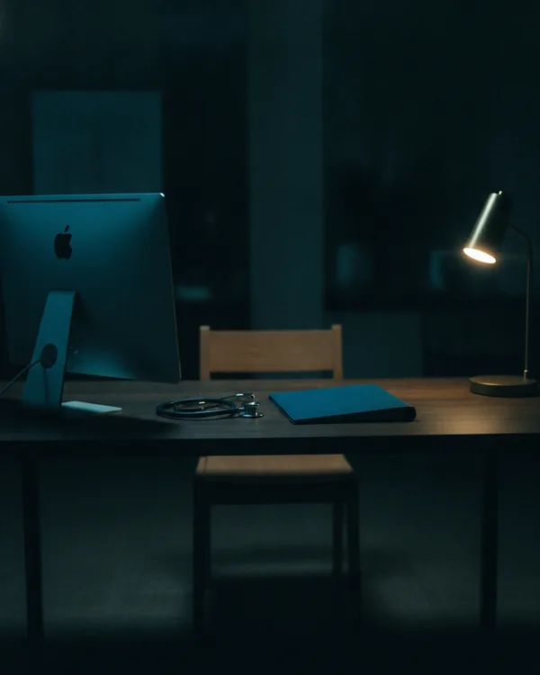 A clinician's desk at night, a monitor glowing beside a coiled stethoscope.