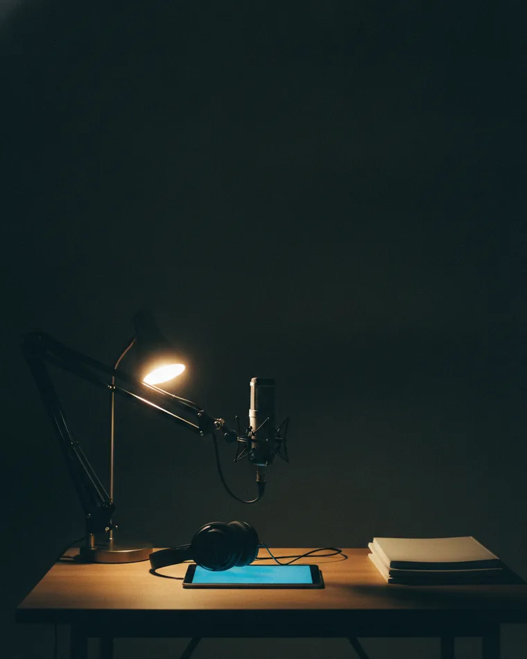 A microphone on a boom arm over a small desk with headphones, a tablet and blank workbooks.