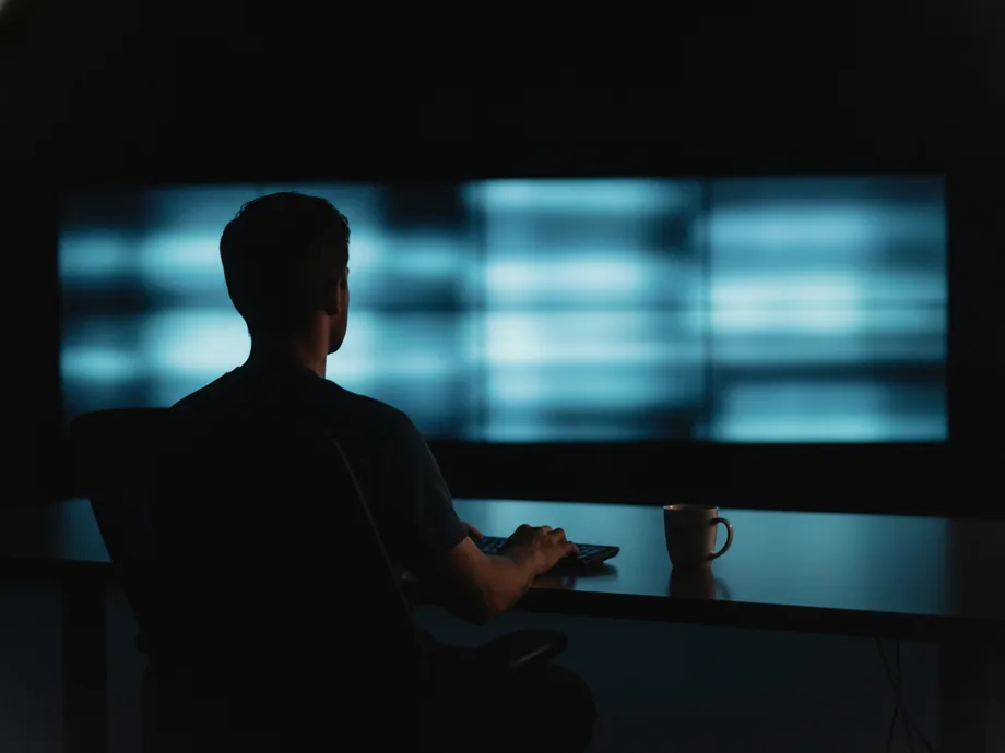 An engineer alone at night watching a wall of dim monitoring displays.