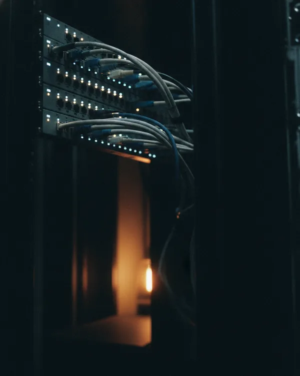 Cable bundles curving into a patch panel in a dark rack, indicator lights glowing.