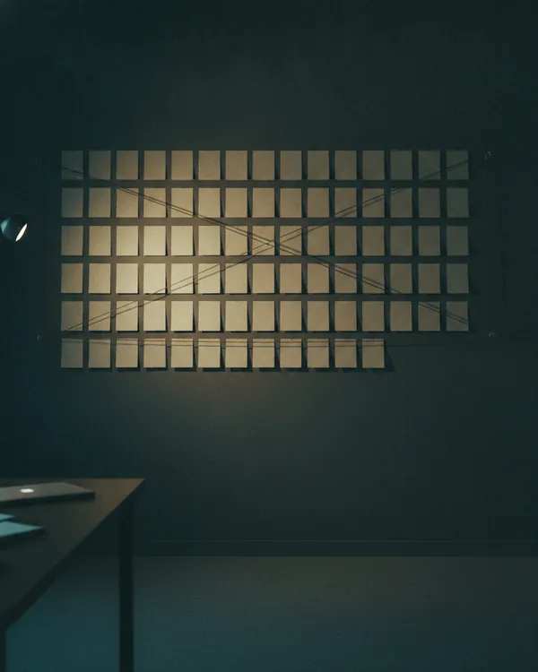 A wall grid of blank index cards crossed by string, lit by a single warm lamp.