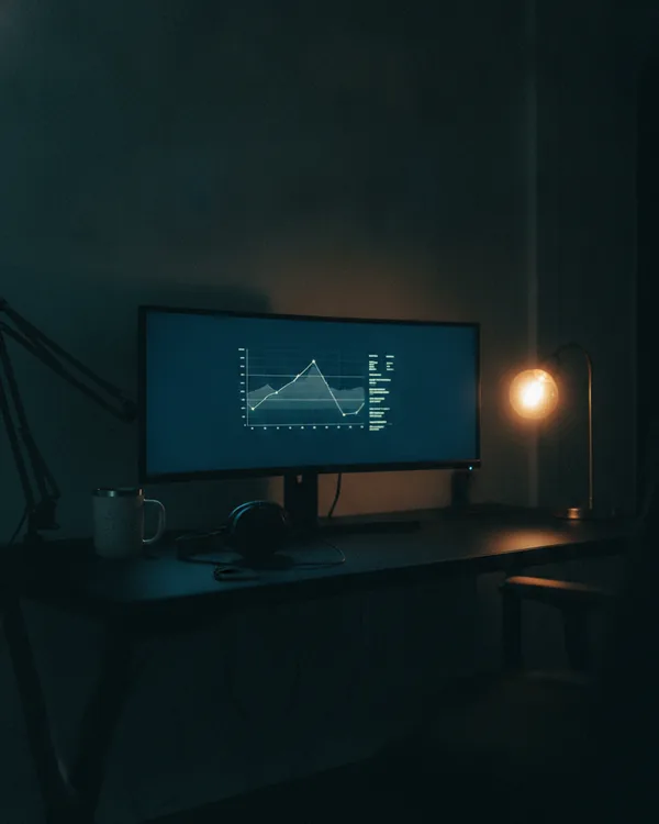 A night desk with a monitor of soft line graphs, a headset and a cooling mug.