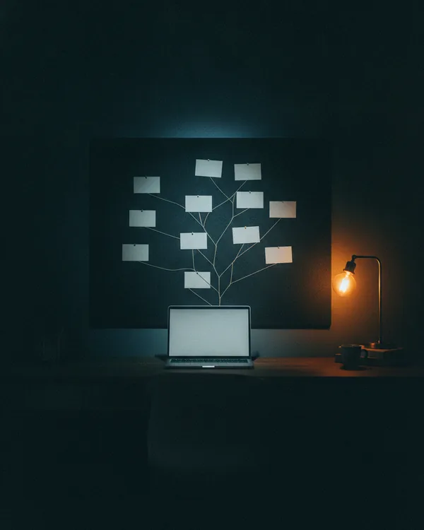 A pinboard tree of blank cards joined by string, lit from a laptop below.