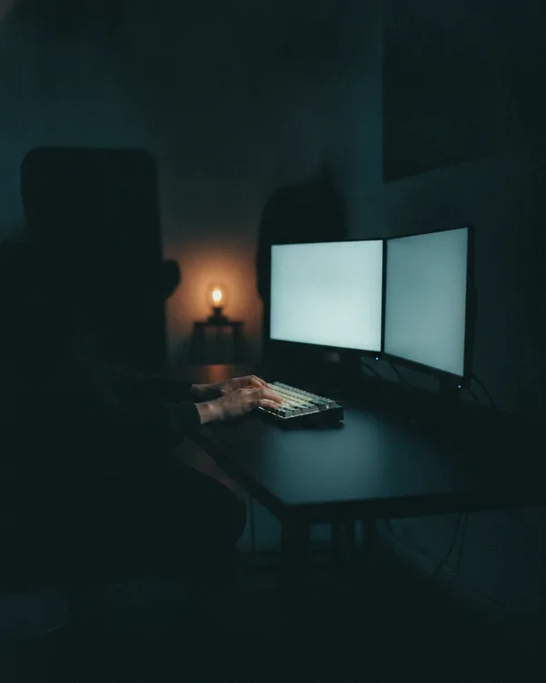 Hands on a mechanical keyboard at a dark desk in front of two glowing monitors.