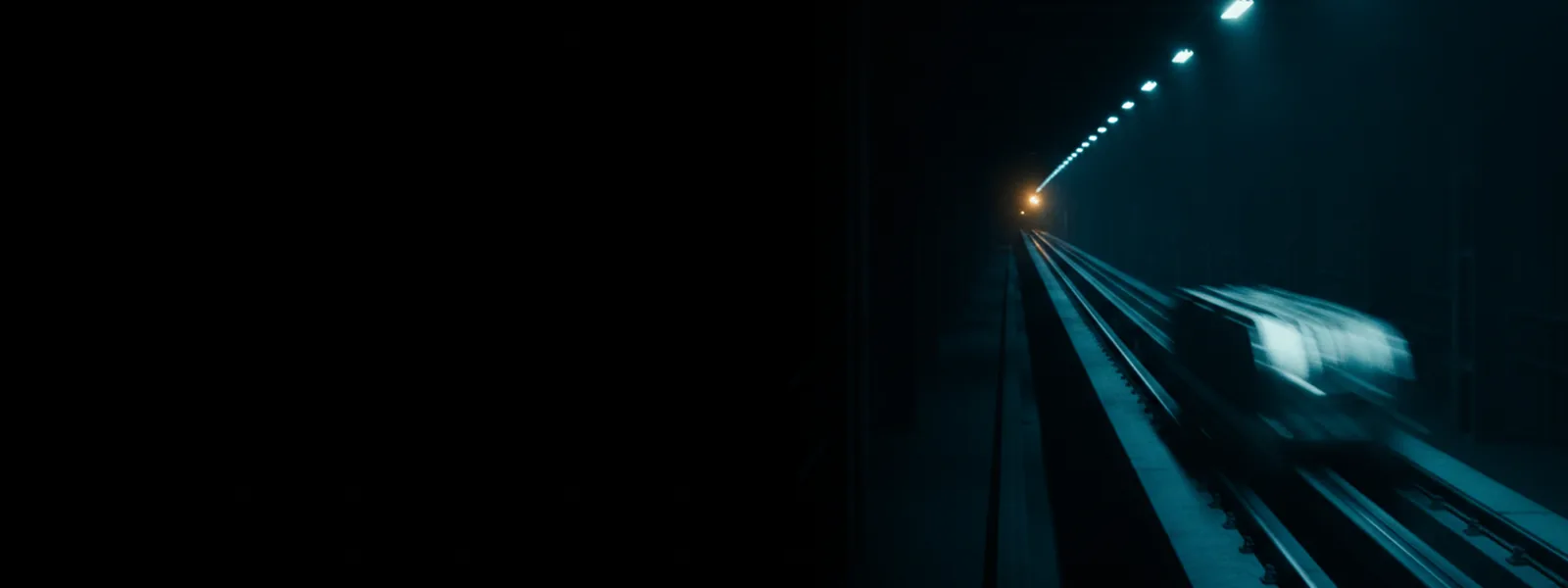 A long factory rail running into depth with one carrier travelling along it under repeating status lamps.